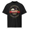 Seoul Emblem Tee, front: a gold-and-red Seoul crest with a palace gate and Namsan Tower on a black oversized tee